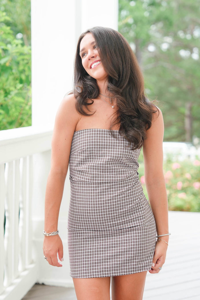 Woman wearing a strapless checkered dress standing on a porch with greenery in the background