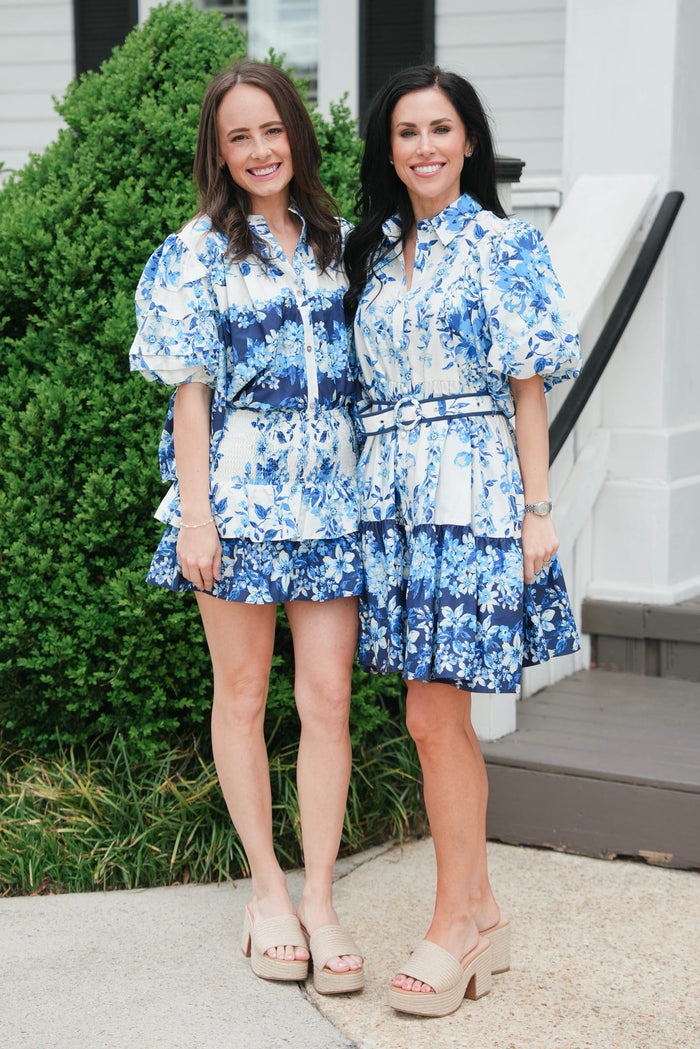 Two women wearing matching blue floral outfits standing on a porch.