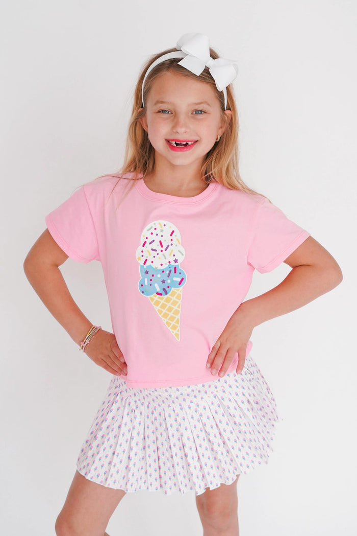 Young girl wearing a pink t-shirt with an ice cream cone design and a white skirt on a light background