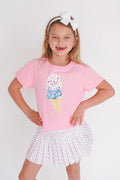 Young girl wearing a pink t-shirt with an ice cream cone design and a white skirt on a light background