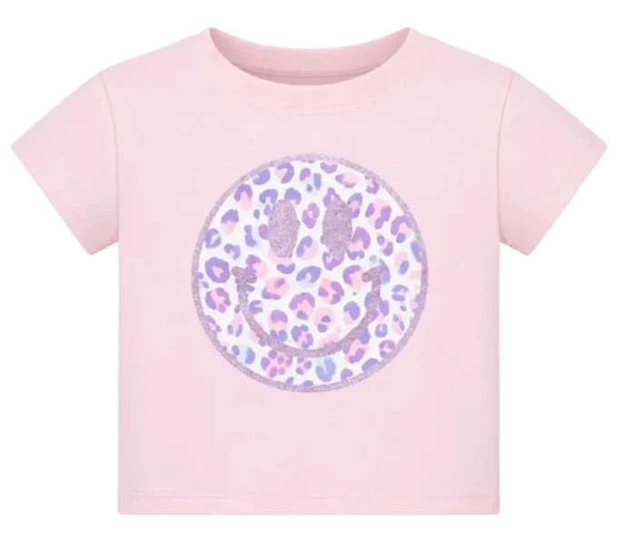 A light pink short-sleeve t-shirt featuring a large circular smiley face graphic on the front. The smiley face has a leopard print pattern in shades of purple, lavender, and pink on a white background, with a glittery pink border.