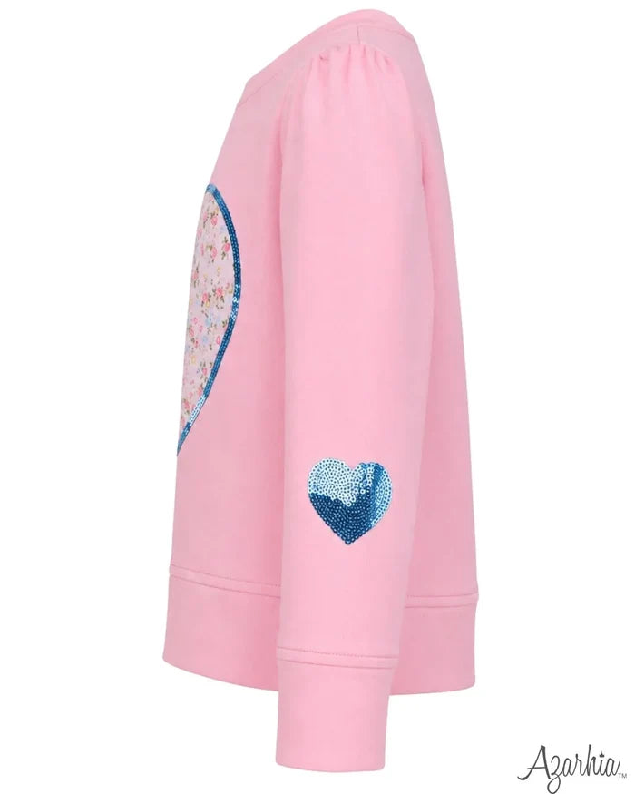 A pink long-sleeve sweatshirt shown from the side, featuring a large sequined heart on the back and a smaller blue sequined heart on the sleeve. The brand name 'Agarkia' is visible in the bottom right corner.