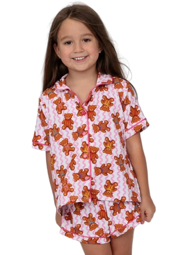 A young girl smiling while wearing a two-piece pajama set. The pajama set features a pink and white chevron pattern with orange teddy bears printed all over it.