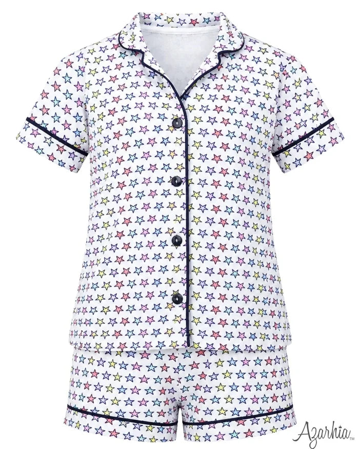 A short-sleeve pajama set with a white base covered in a colorful star pattern, featuring dark navy piping along the collar, placket, cuffs, and hem. The set includes a button-front top and matching shorts.