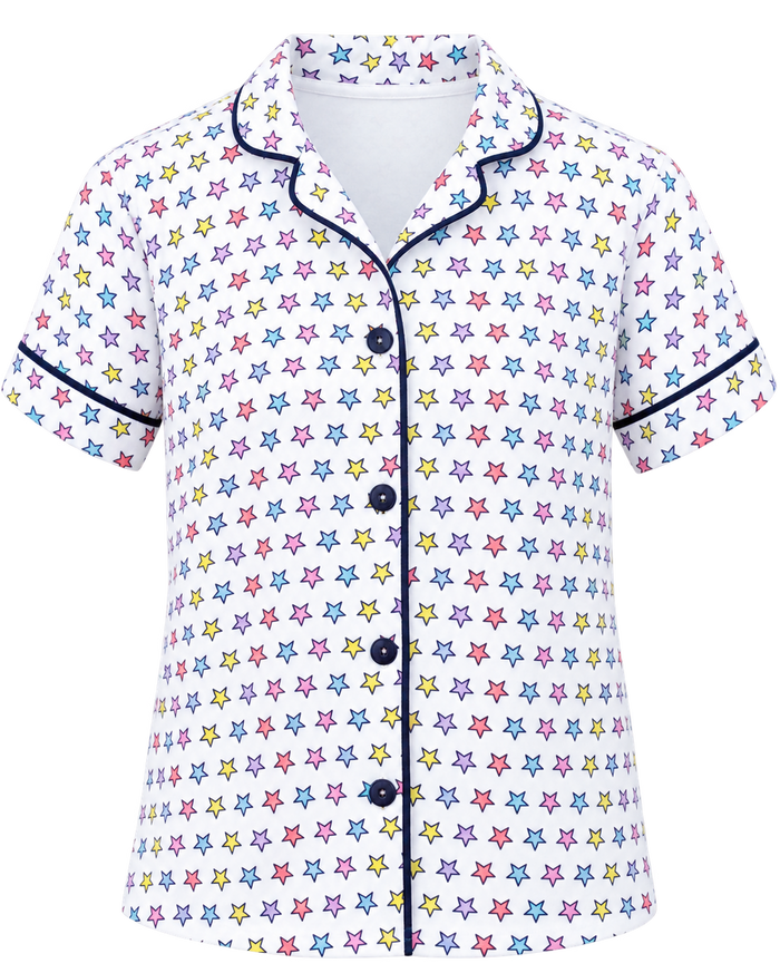 A short-sleeve button-front pajama shirt with an all-over multicolor star print on a white base, featuring dark navy piping along the collar, placket, cuffs, and hem.