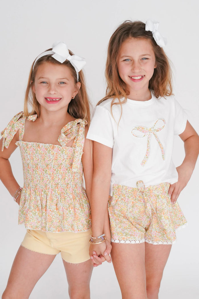 Two young girls wearing matching outfits with floral tops and shorts on a white background