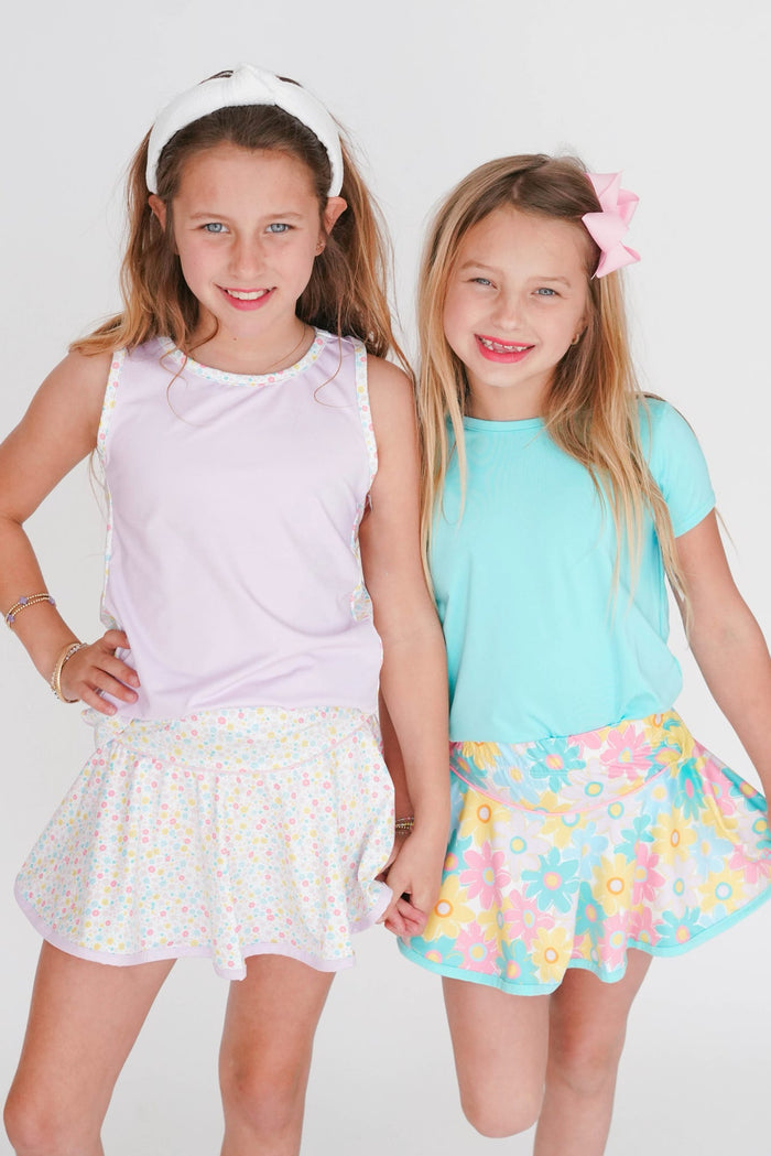 Two young girls wearing pastel-colored outfits with floral skirts on a white background
