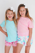 Two young girls wearing colorful outfits with matching accessories on a white background
