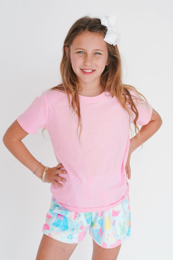 Young girl wearing a pink shirt and colorful shorts with a white background