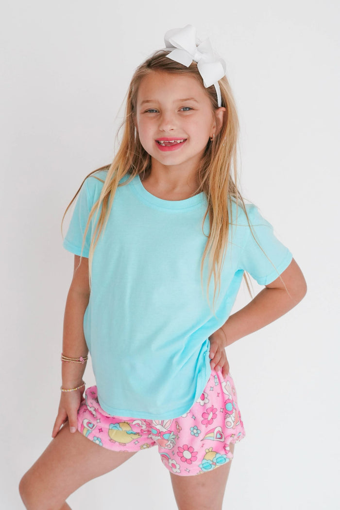 Young girl wearing a light blue shirt and pink shorts with a white background