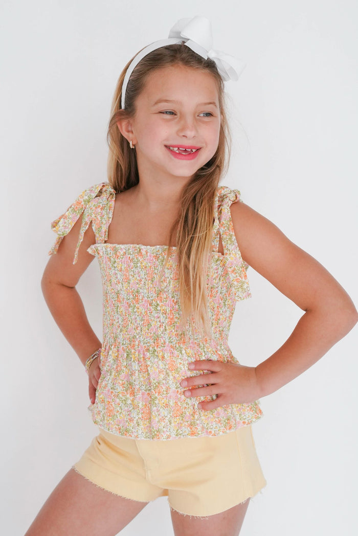 Young girl wearing a floral top and yellow shorts on a white background