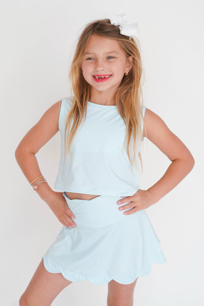 Young girl wearing a light blue sleeveless top and skirt set on a white background
