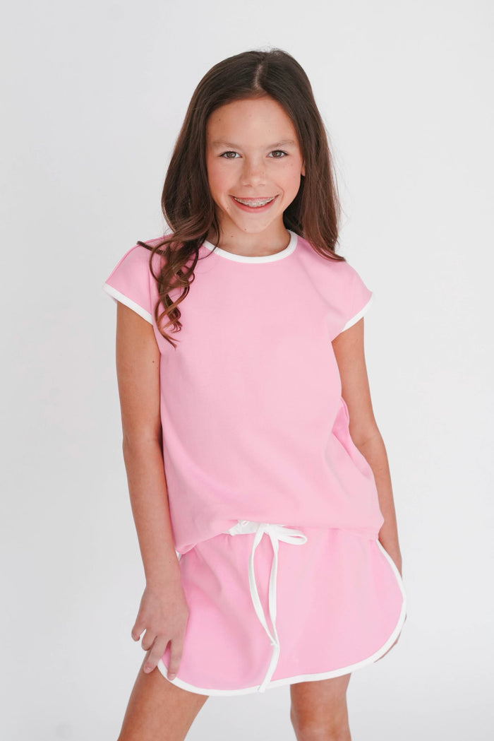 Young girl wearing a pink dress with white trim on a plain background