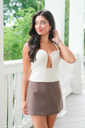 Woman wearing a white top with a cutout design and a brown skirt on a porch.
