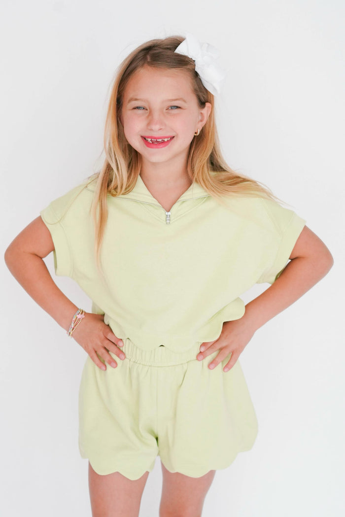 Young girl wearing a light green romper against a white background