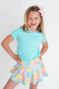 Young girl wearing a light blue top and floral skirt with a white background