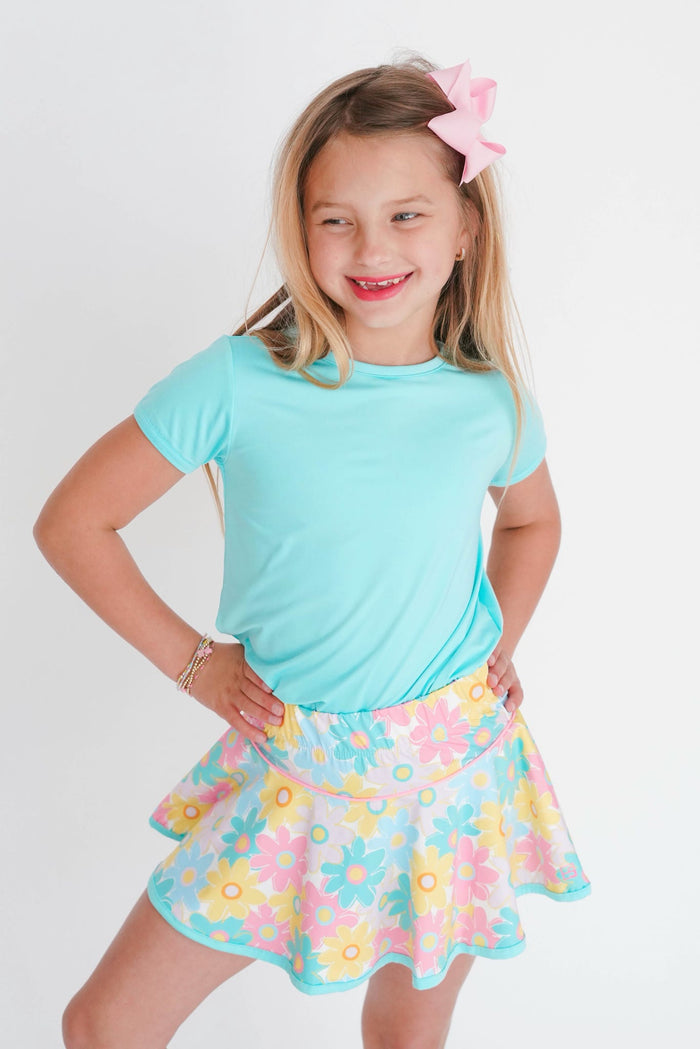 Young girl wearing a light blue t-shirt and a colorful floral skirt on a white background