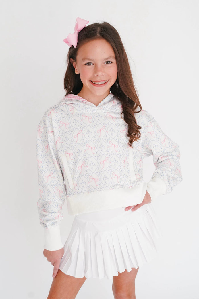 Young girl wearing a white floral hoodie and white skirt with a pink bow in her hair on a white background