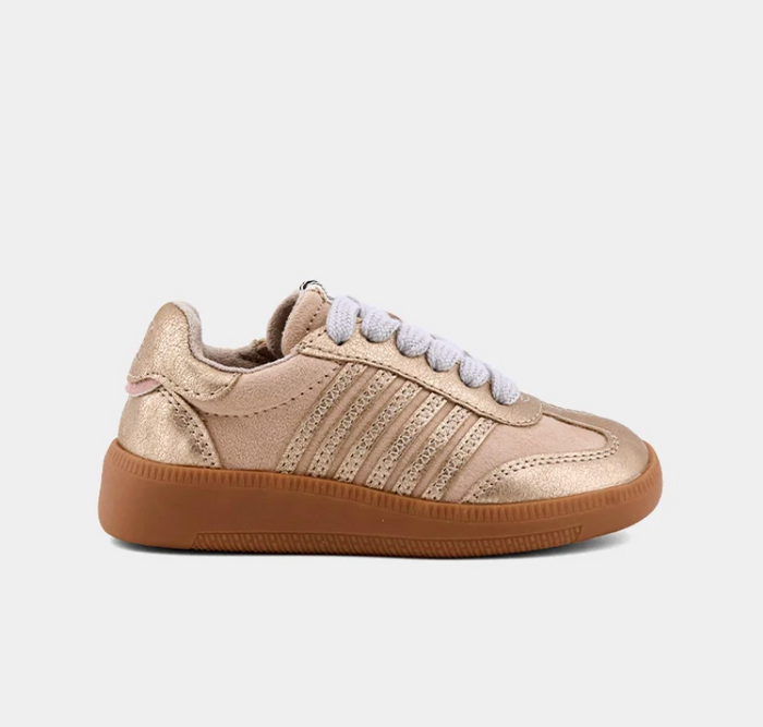 A low-top sneaker in metallic gold with white laces and a brown gum sole, shown from a side profile on a light gray background.