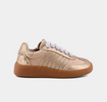 A low-top sneaker in metallic gold with white laces and a brown gum sole, shown from a side profile on a light gray background.