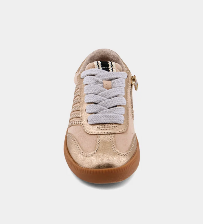 A single low-top sneaker shown from a front-facing overhead angle on a light gray background. The shoe has a metallic champagne-gold upper, light gray laces, a side zipper with a gold pull tab, and a brown gum sole.
