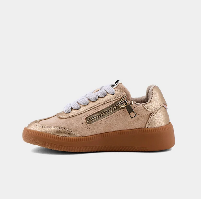 A low-top sneaker in metallic gold with a brown gum sole, white laces, and a side zipper, shown from a side profile on a light gray background.