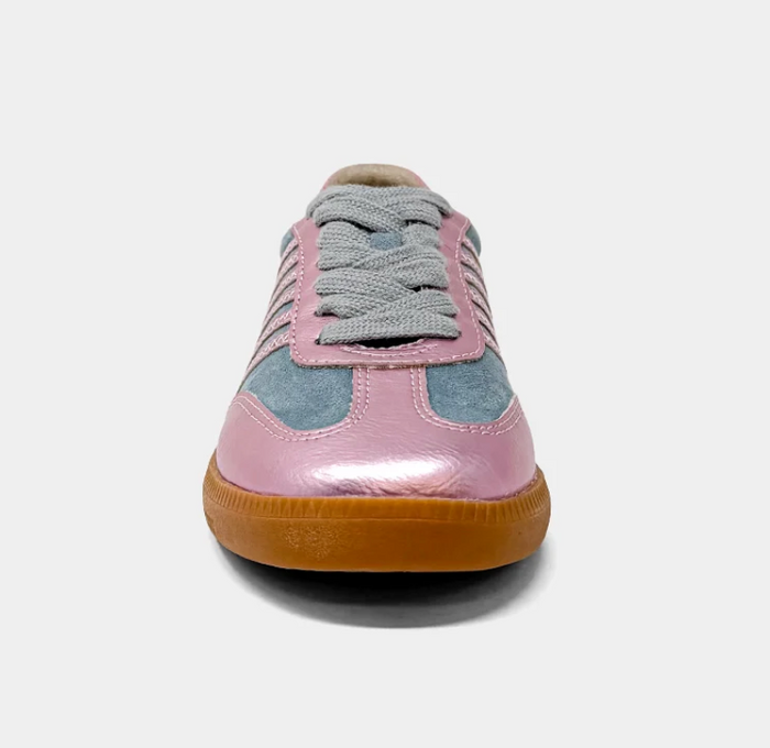 A single low-top sneaker shown from the front on a light gray background. The shoe features a glossy light pink leather toe cap, dusty blue suede side panels, a light gray knit lace overlay, and a brown gum rubber sole.