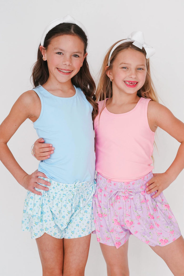Two young girls wearing matching outfits with light blue and pink tops and floral shorts on a white background.
