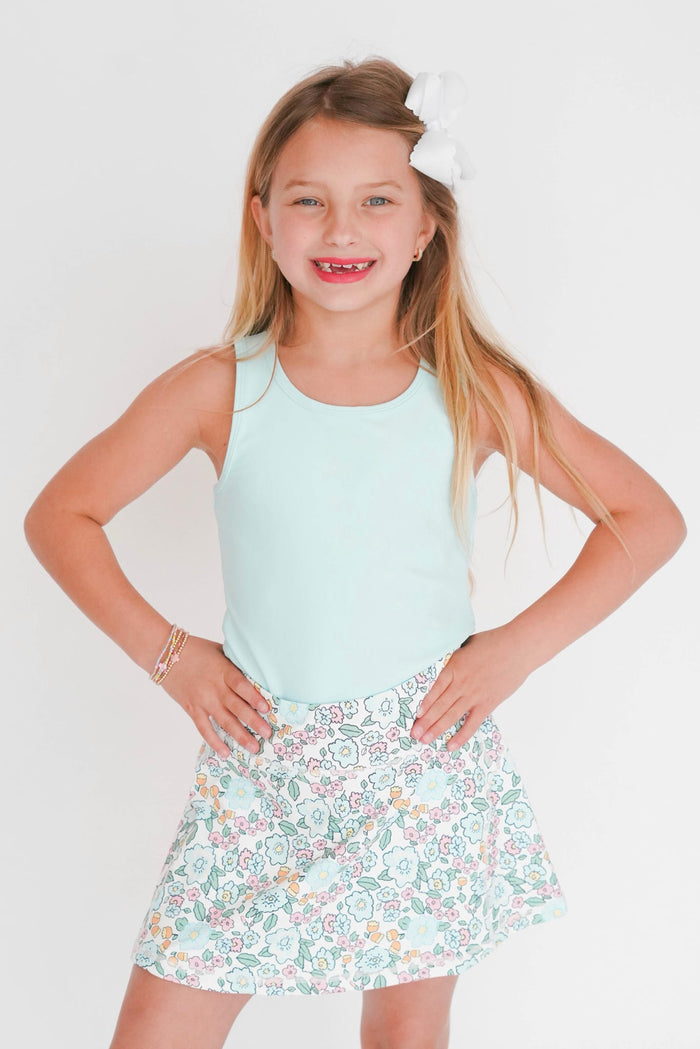 Young girl wearing a light blue sleeveless top and floral skirt on a white background