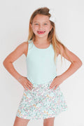 Young girl wearing a light blue sleeveless top and floral skirt on a white background