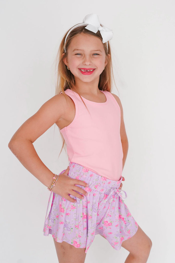 Young girl wearing a pink sleeveless top and floral skirt on a white background