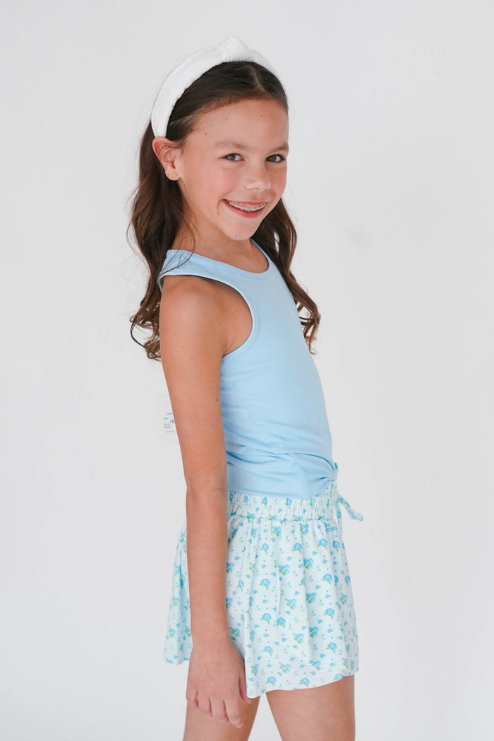 Young girl wearing a light blue sleeveless top and floral skirt on a white background