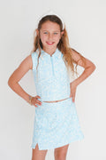 Young girl wearing a light blue floral dress with a white headband against a plain background