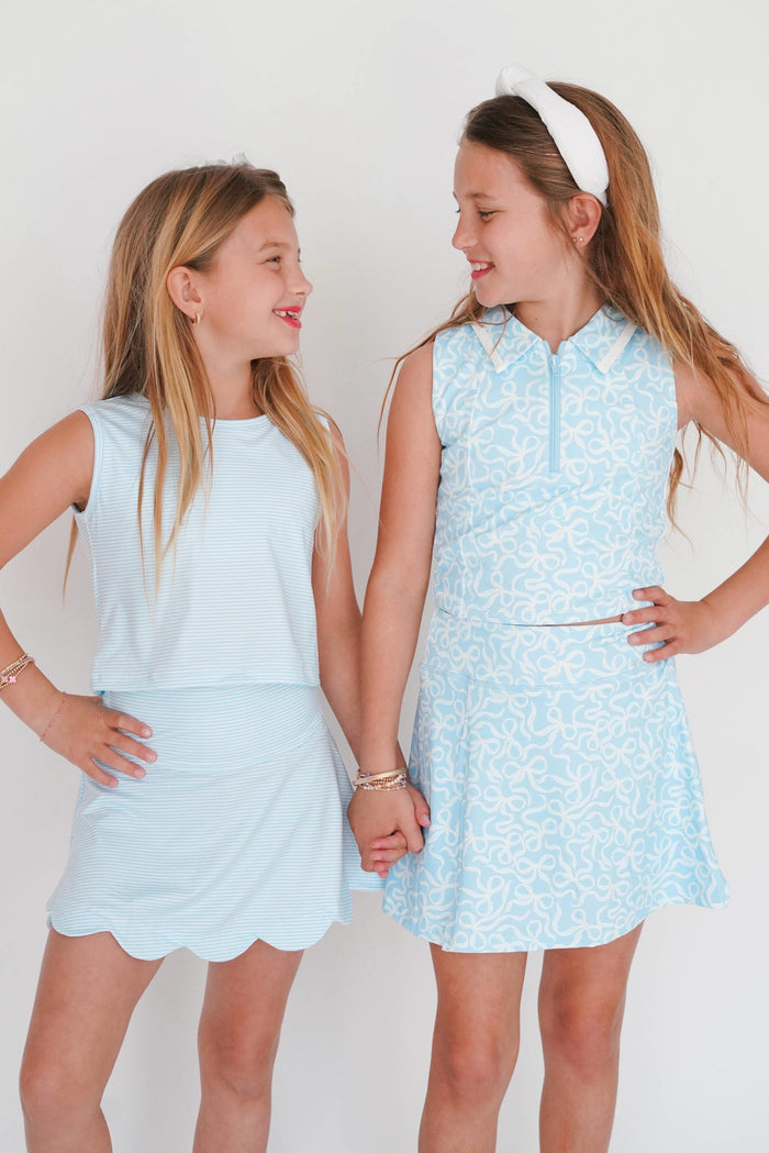 Two young girls wearing light blue dresses standing against a white background