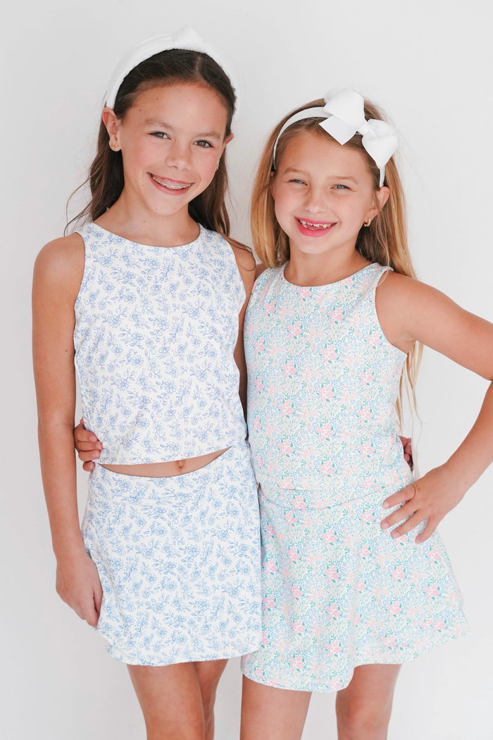 Two young girls wearing matching light blue floral outfits against a white background