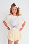 Young girl wearing a white t-shirt with graphics and text, standing against a plain background