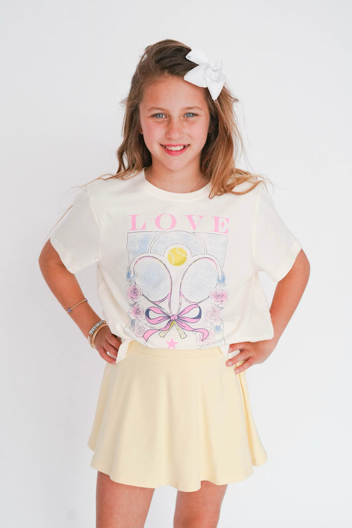 Young girl wearing a white t-shirt with graphics and text, standing against a plain background