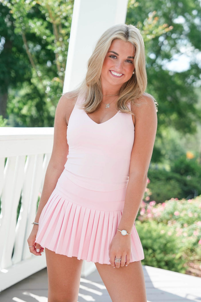 Woman in a pink dress standing outdoors with greenery in the background