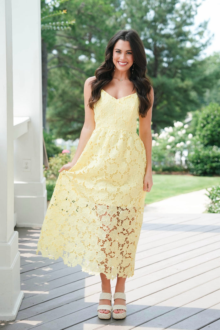 Woman in a yellow lace dress standing on a wooden deck with greenery in the background