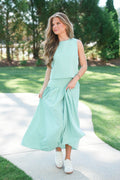 Woman wearing a light green sleeveless top and skirt set on a sunny day outdoors.