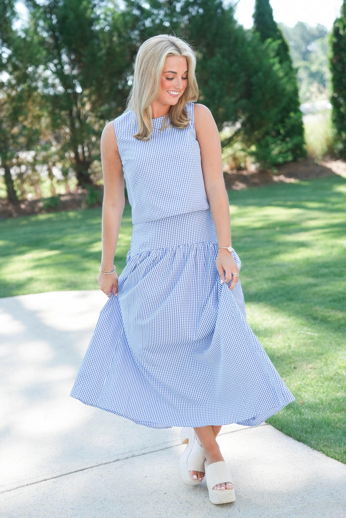 Woman wearing a blue checkered dress standing outdoors on a sunny day.