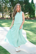 Woman in a light blue dress standing on a path with greenery in the background