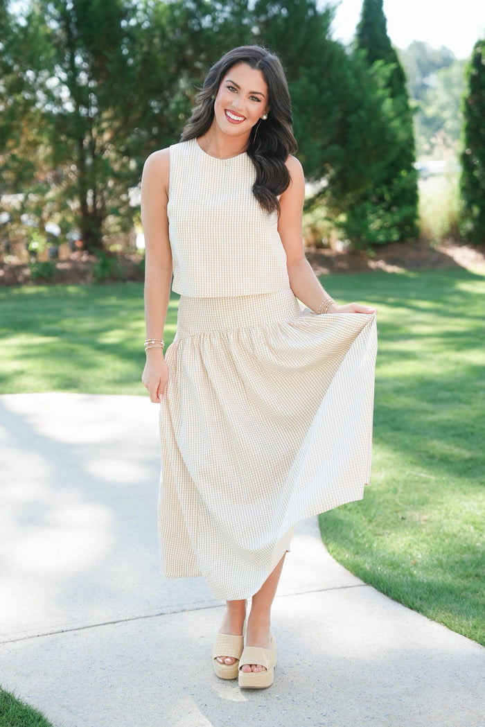Woman in a white dress standing on a sidewalk with greenery in the background