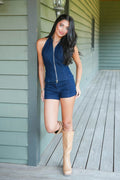 A woman posing on a wooden porch wearing a dark blue denim halter top and matching denim shorts, paired with tan knee-high boots.