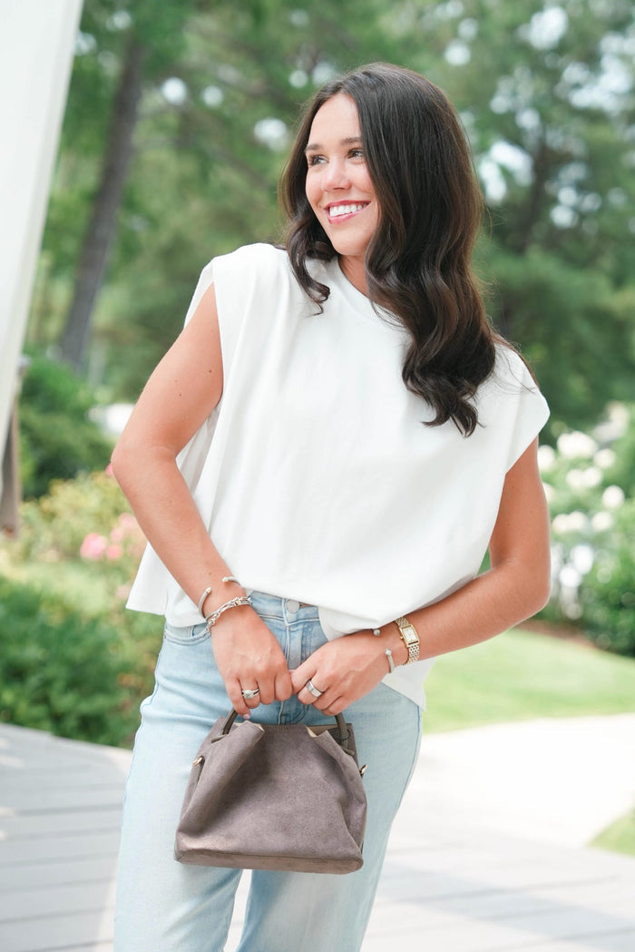 Woman in a white blouse and light blue jeans holding a brown handbag outdoors.