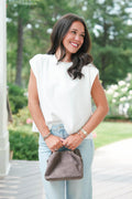 Woman in a white blouse and light blue jeans holding a brown handbag outdoors.