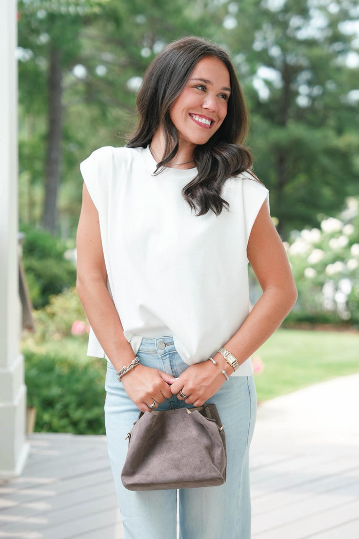 Woman in a white blouse and light blue jeans holding a brown handbag outdoors.