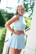 Woman wearing a light blue two-piece outfit standing outdoors with greenery in the background