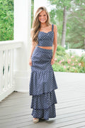 Woman wearing a navy blue polka dot dress on a wooden deck with greenery in the background