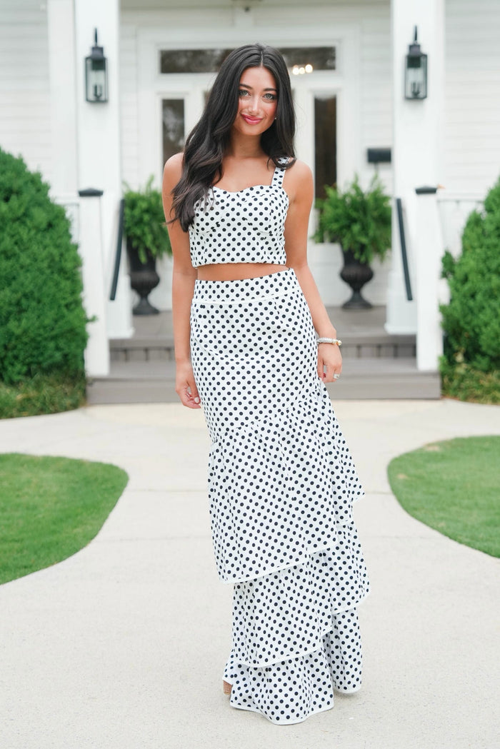 Woman wearing a black and white polka dot dress standing in front of a white house.